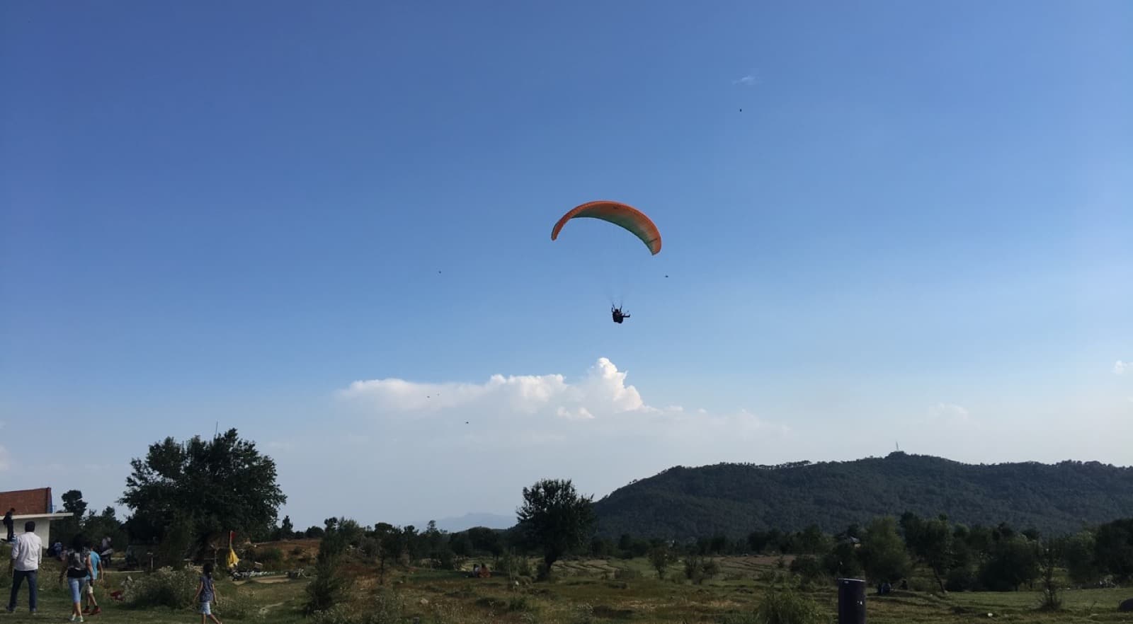 Paraglider above the Bir Billing landing area with low hills in late light